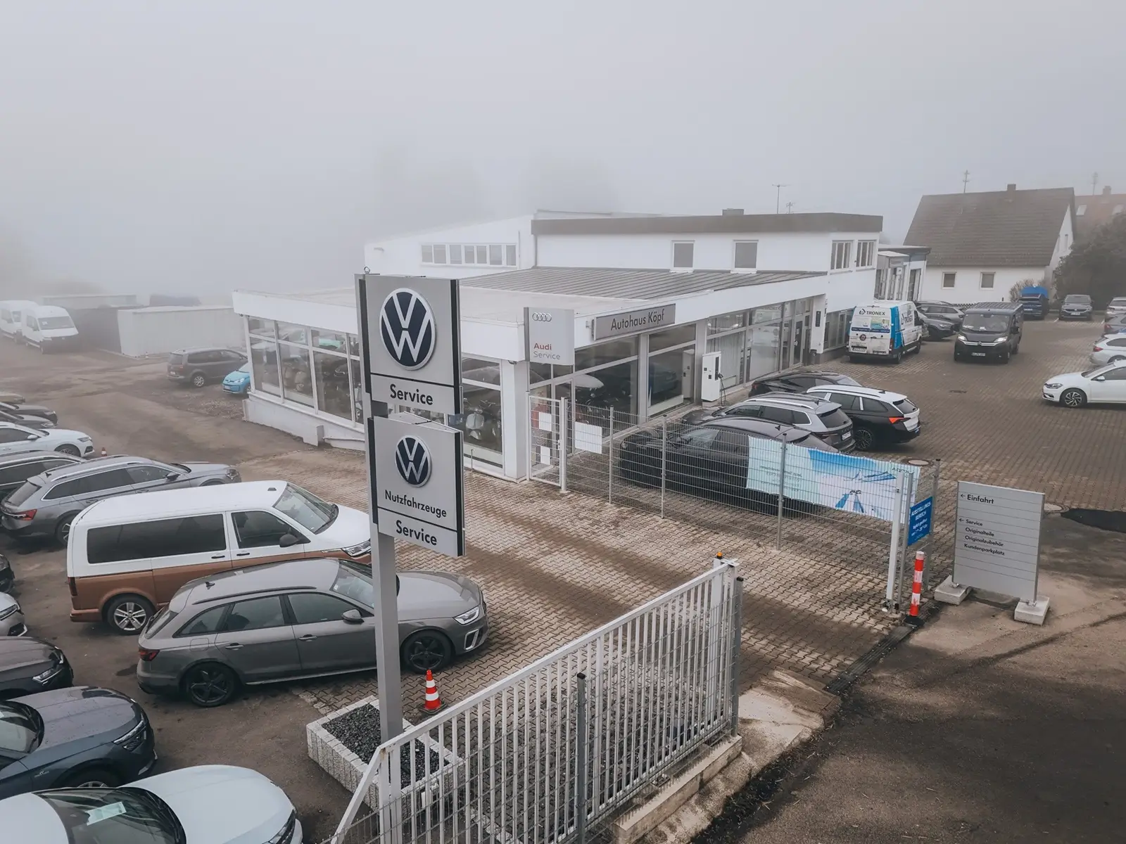 Außenaufnahme des Autohaus Köpf in Röfingen an einem nebligen Tag mit sichtbaren VW-Schildern und Fahrzeugen auf dem Gelände